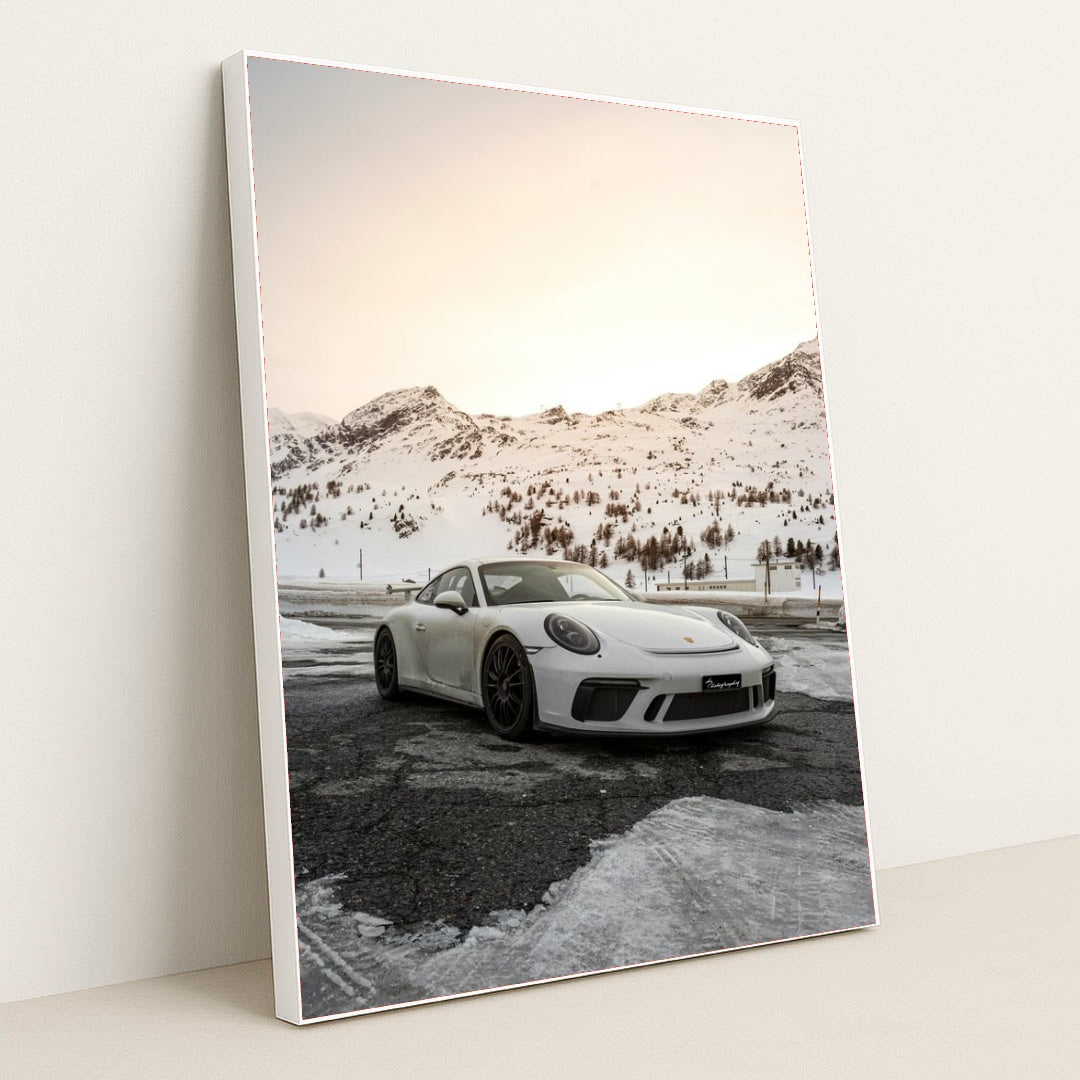 This photo shows a white Porsche sports car parked on a snow-covered mountain road at sunset, in a white frame.