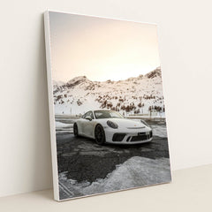 This photo shows a white Porsche sports car parked on a snow-covered mountain road at sunset, in a white frame.