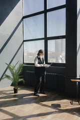 Mikhail Nilov - A person standing by large windows in a modern office, working on a laptop.