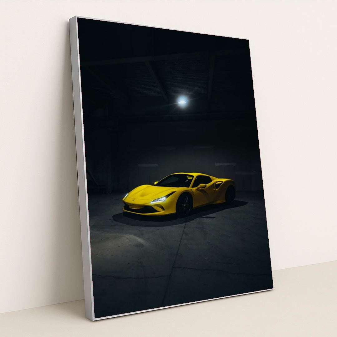 This photo shows a yellow Ferrari sports car spotlighted in a dark, empty garage, in a silver frame.
