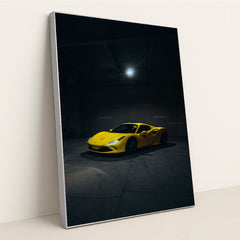 This photo shows a yellow Ferrari sports car spotlighted in a dark, empty garage, in a silver frame.