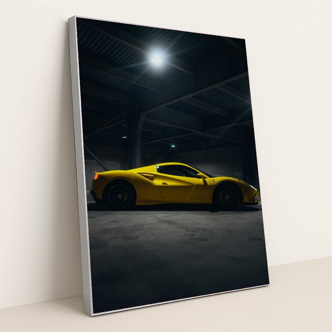 This photo shows a yellow Ferrari sports car in a dimly lit industrial garage, side view captured under overhead lights, in a silver frame.
