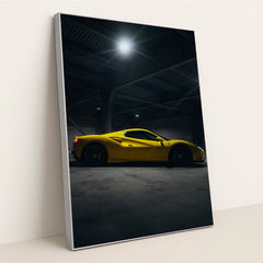 This photo shows a yellow Ferrari sports car in a dimly lit industrial garage, side view captured under overhead lights, in a silver frame.