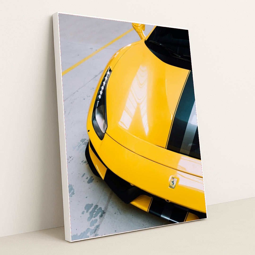 This photo shows the front end of a yellow Ferrari 488 Pista with black and silver racing stripes indoors, in a white frame.