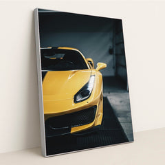 This photo shows the front left side of a yellow Ferrari with sharp headlights and black striping, parked indoors, in a silver frame.