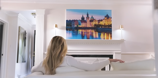 Wall Gusto fabric wall art featuring a colorful European cityscape reflected on a river, displayed above a fireplace mantel in a bright living room