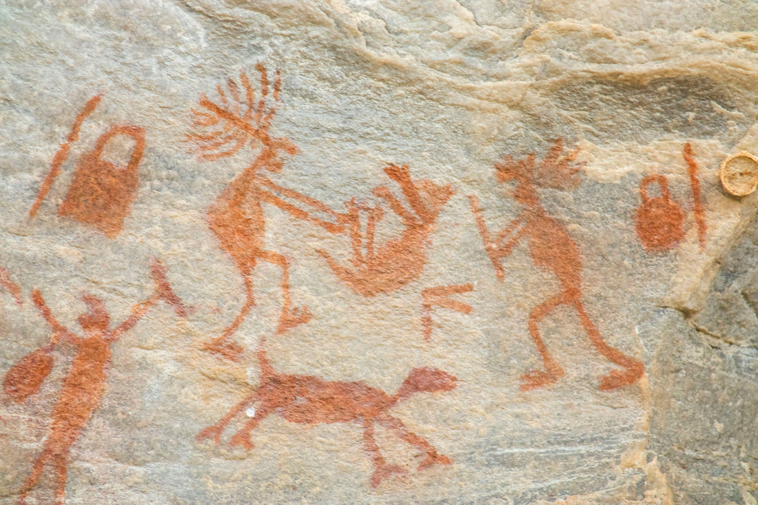 Ancient rock art depicting human figures and animals painted in red pigment on a stone surface