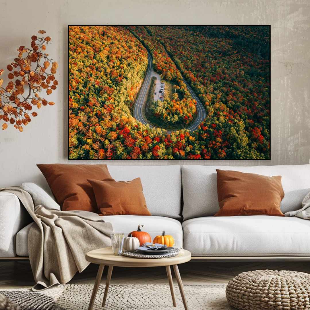 Living room with a large wall art of a winding road through a forest, white sofa with brown and beige pillows, and a small round table.
