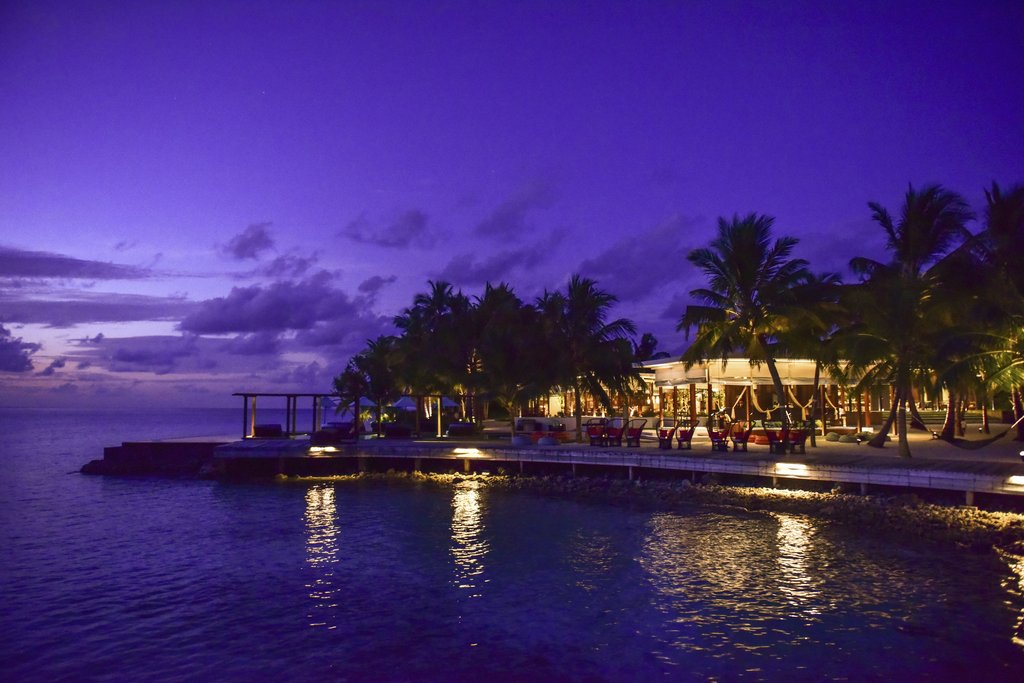 Asad Photo Maldives - A breathtaking view of a tropical resort at twilight, surrounded by palm trees and reflecting on the ocean.