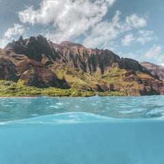 Jess Loiterton - Captivating view of the Na Pali coastline with clear turquoise waters, showcasing dramatic cliffs under a sunny sky.