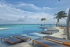Geek Wandering - Relax by the stunning infinity pool at a luxury resort in the Maldives, surrounded by turquoise waters and palm trees.