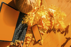 Jakub Zerdzicki - Bright autumn-themed workspace showcasing a laptop, smartphone, pumpkin, and fallen leaves.