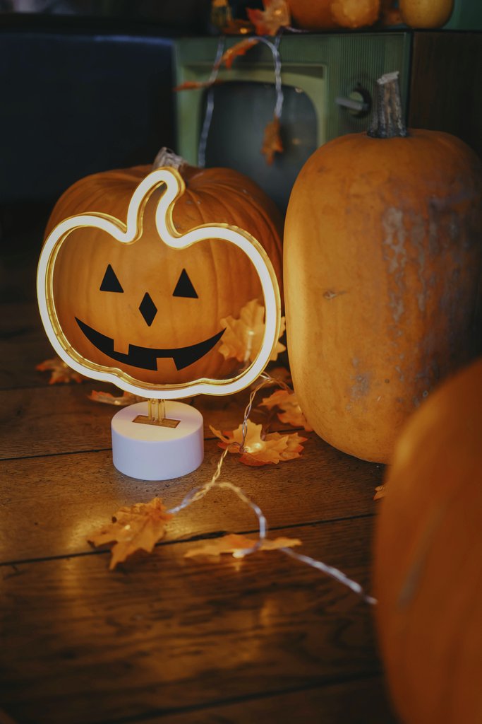 Valeria Boltneva - Charming indoor Halloween scene with pumpkins, warm lighting, and autumn leaves.