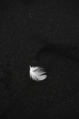 ArtHouse Studio - Top view of small white seabird feather placed on black sand texture background located on famous ocean beach with black and white effect