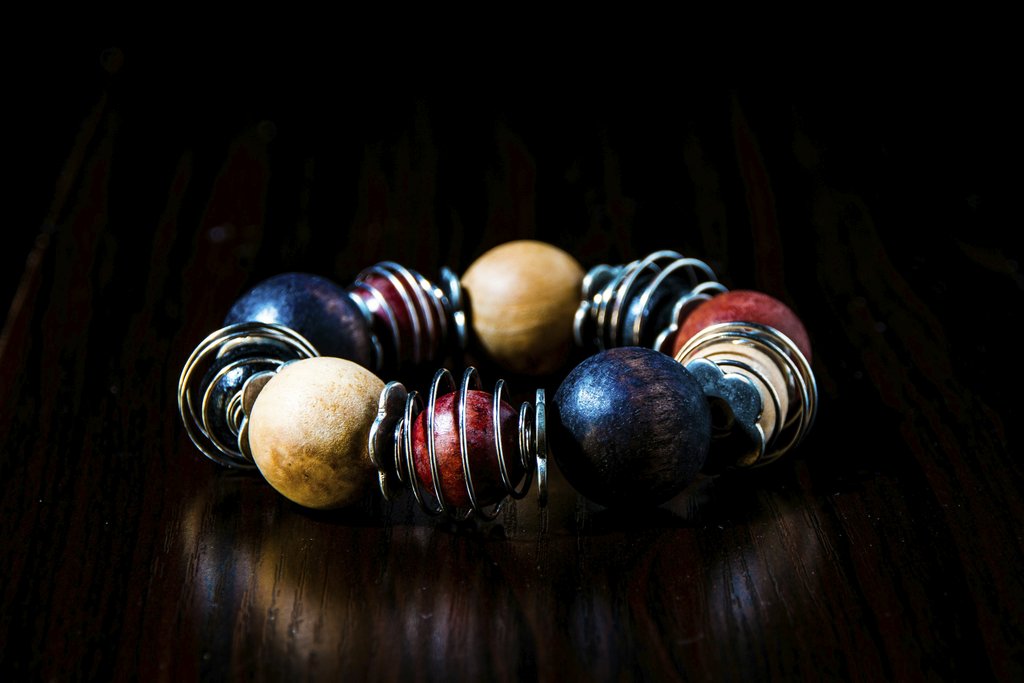 Ellis Mbeku - Close-up of a vibrant wood bead bracelet with metallic spiral accents on a dark background.