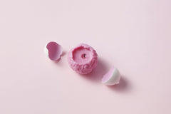 DS stories - A unique pink candle shaped like a brain surrounded by white eggshells on a light pink background.