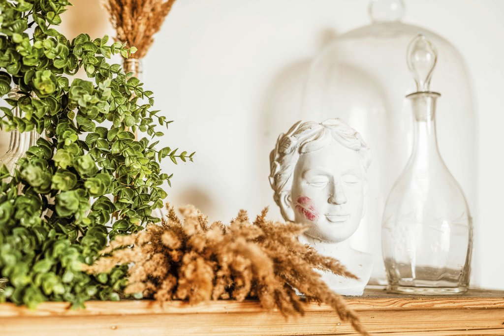 Helena Jankovičová Kováčová - A serene still life featuring a bust with lipstick traces, boxwood, dried grass, and a glass carafe.