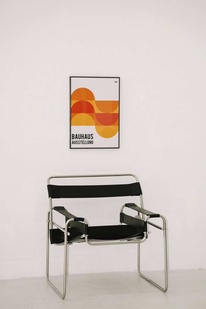 Ricky Esquivel - Bauhaus poster with geometric design above a sleek black chair against a white wall.