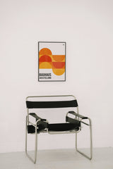 Ricky Esquivel - Bauhaus poster with geometric design above a sleek black chair against a white wall.