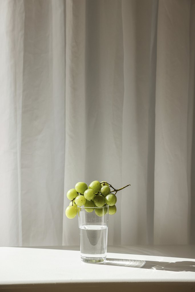Cup of  Couple - A serene still life featuring green grapes on a glass of water against a curtain backdrop.