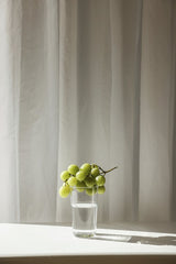 Cup of  Couple - A serene still life featuring green grapes on a glass of water against a curtain backdrop.