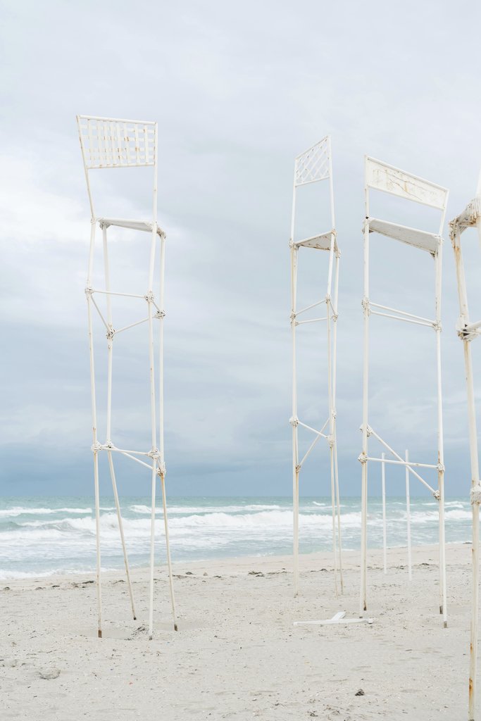 Mikhail Nilov - Tall metal structures stand gracefully against a calming beach backdrop with soothing ocean waves.