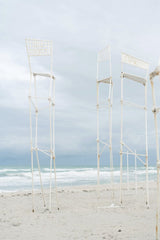 Mikhail Nilov - Tall metal structures stand gracefully against a calming beach backdrop with soothing ocean waves.
