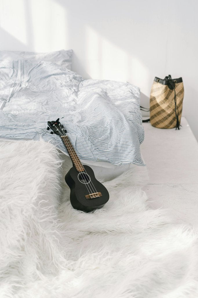Mikhail Nilov - A tranquil bedroom setting featuring a ukulele on a plush white rug, perfect for relaxation.