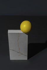 Mikhail Nilov - A striking still life featuring a yellow sphere balanced on a marble cube against a dark backdrop.