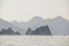 Julia Volk - A tranquil view of rocky coastal mountains reflecting on calm water at dusk, surrounded by a pastel sky.