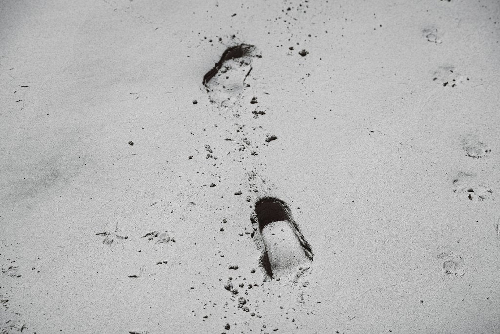 ROMAN ODINTSOV - Black and white image of footprints in the sand, showcasing solitude and journey.