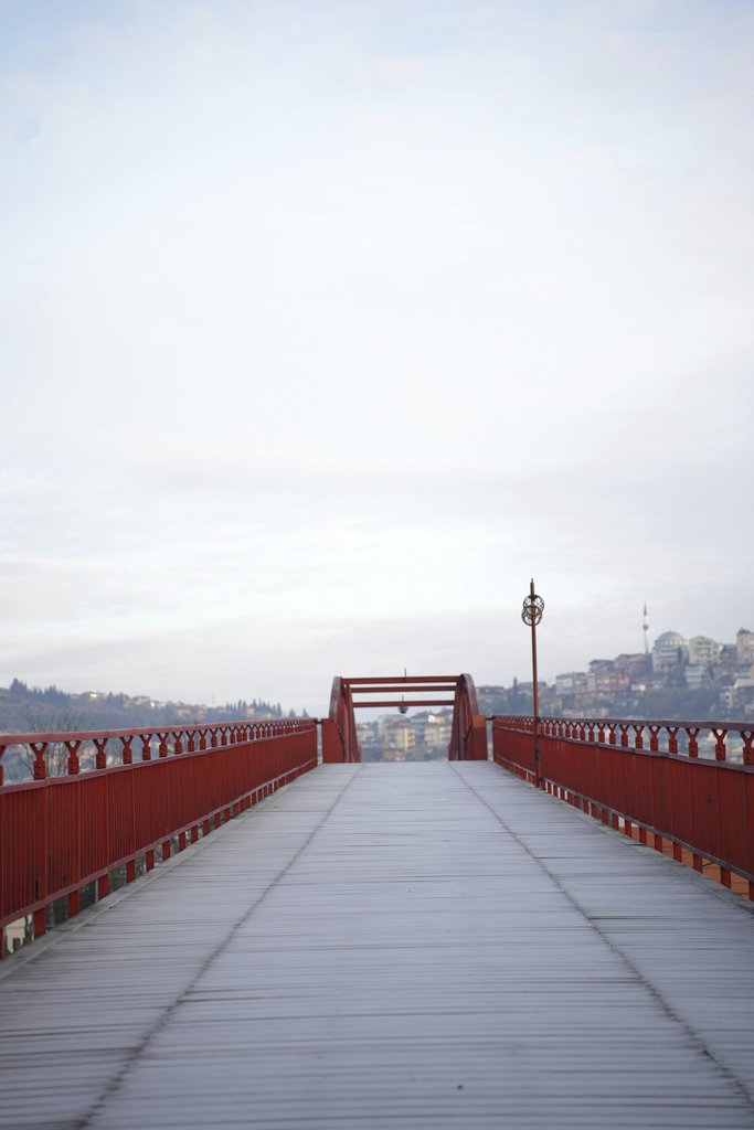 zeynep şahin - Long red metal bridge leading to distant cityscape under clear sky.