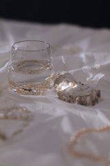 cottonbro studio - A serene still life featuring a glass of water, seashell, and pearls on white fabric.
