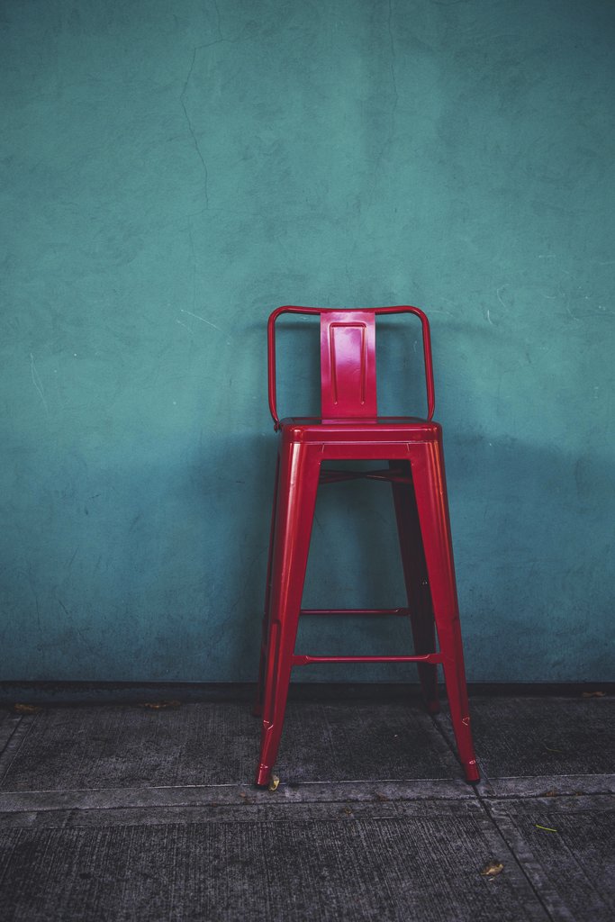 Tim Mossholder - A striking red metal stool stands against a vibrant teal wall in an urban outdoor setting in Portland, Oregon.