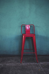 Tim Mossholder - A striking red metal stool stands against a vibrant teal wall in an urban outdoor setting in Portland, Oregon.