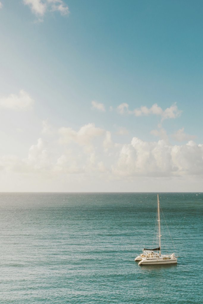 Jess Loiterton - A solitary sailboat floats on a tranquil sea under a bright blue sky.