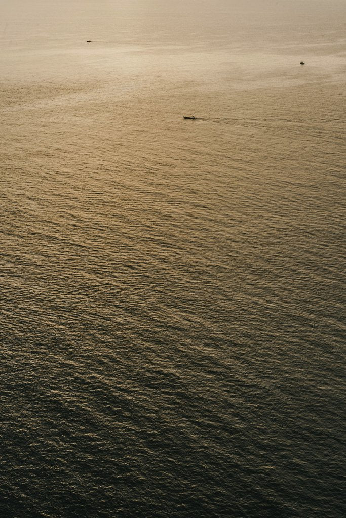 Alesia  Kozik - A tranquil view of the ocean at sunset with small boats in Bali, Indonesia.