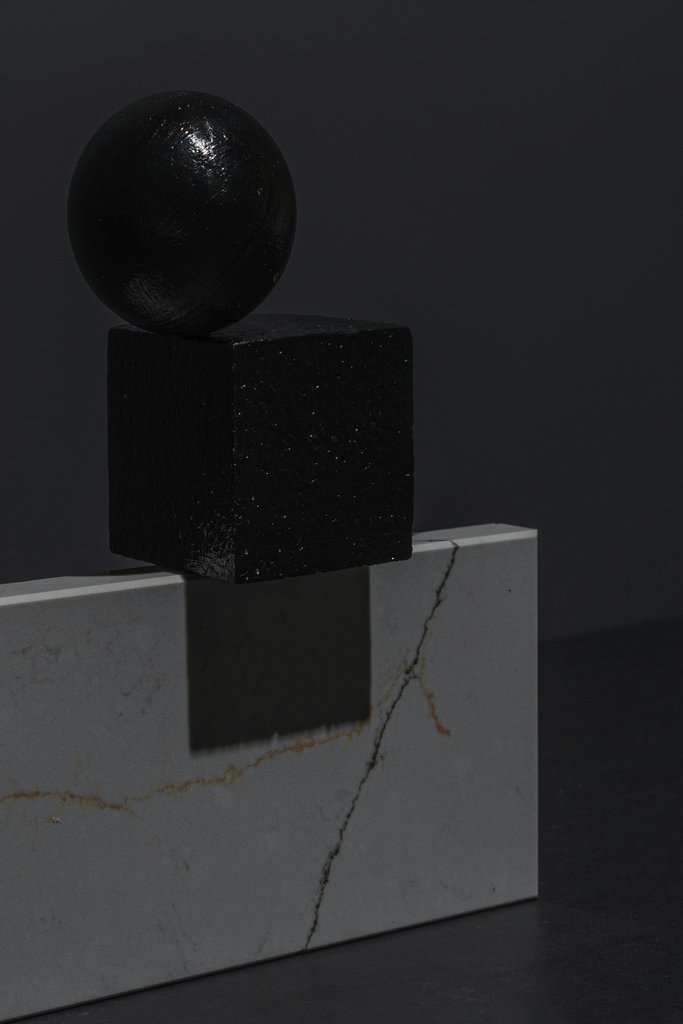 Mikhail Nilov - Black geometric sphere and cube on a marble slab, showcasing minimalist design and contrast.