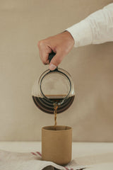 Cup of  Couple - A close-up image of a hand pouring coffee from a glass pitcher into a cup on a neutral background.