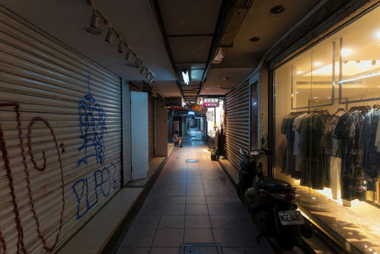 Jimmy Liao - Dimly lit urban alleyway with graffiti walls and a clothing store at night.