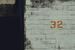 Connor McManus - An aged urban wall featuring the number 32 in orange graffiti, offering a gritty cityscape aesthetic.