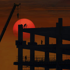 大伟 - Silhouette of a construction site with workers against a dramatic sunset backdrop.
