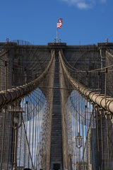 Fatih Turan - Iconic Brooklyn Bridge showcasing its architectural details with a waving American flag against a clear blue sky.