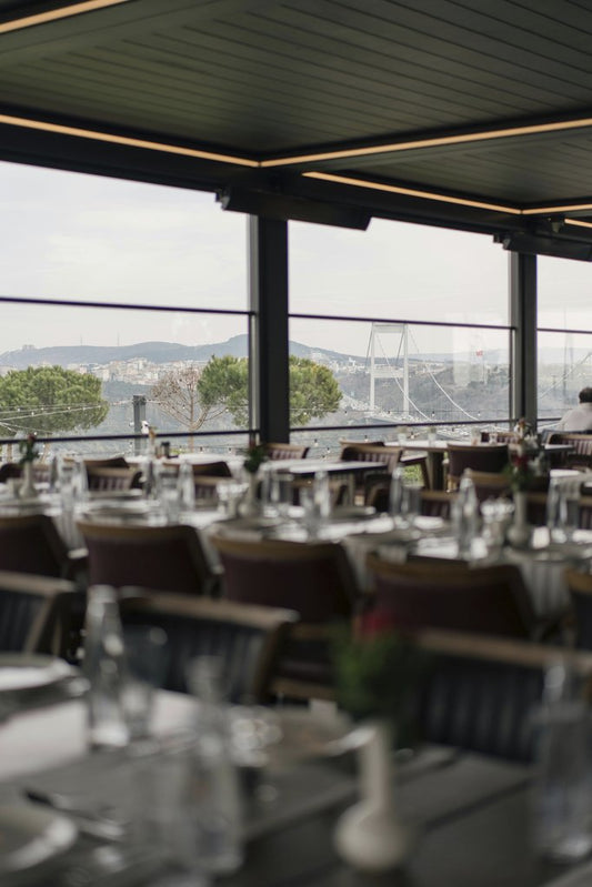 Gül Işık - Elegant restaurant interior with a view of a city skyline through large windows.