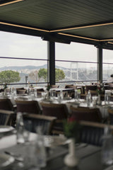 Gül Işık - Elegant restaurant interior with a view of a city skyline through large windows.