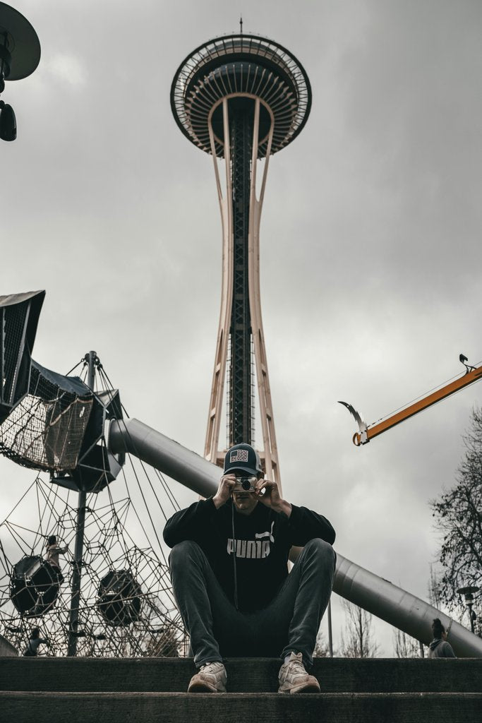J3 Media Group - Man sitting in front of Seattle's Space Needle on an overcast day.