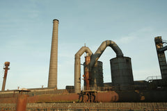 Willian Matiola - An abandoned and rusty factory with towering chimneys under a clear sky.
