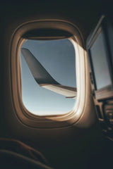 Afif Ramdhasuma - A scenic view of an airplane wing through a window, flying high above the clouds.