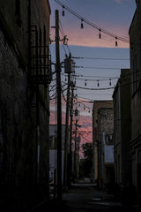 Connor McManus - Silhouetted urban alleyway with string lights against a vibrant sunset sky.
