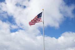 Ira Bowman - The American flag flutters against a blue sky with fluffy white clouds, symbolizing patriotism.